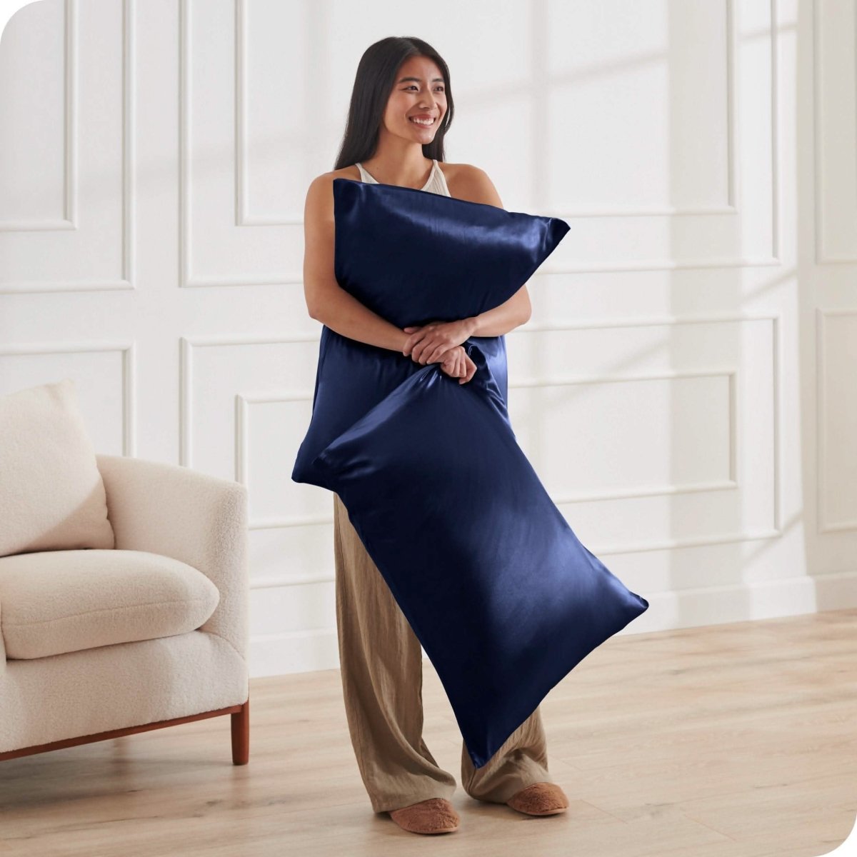 A woman standing while holding pillows with silk pillowcases on them
