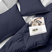 Close up of a comforter set on a bed. There are glasses and a magazine on top of the comforter.