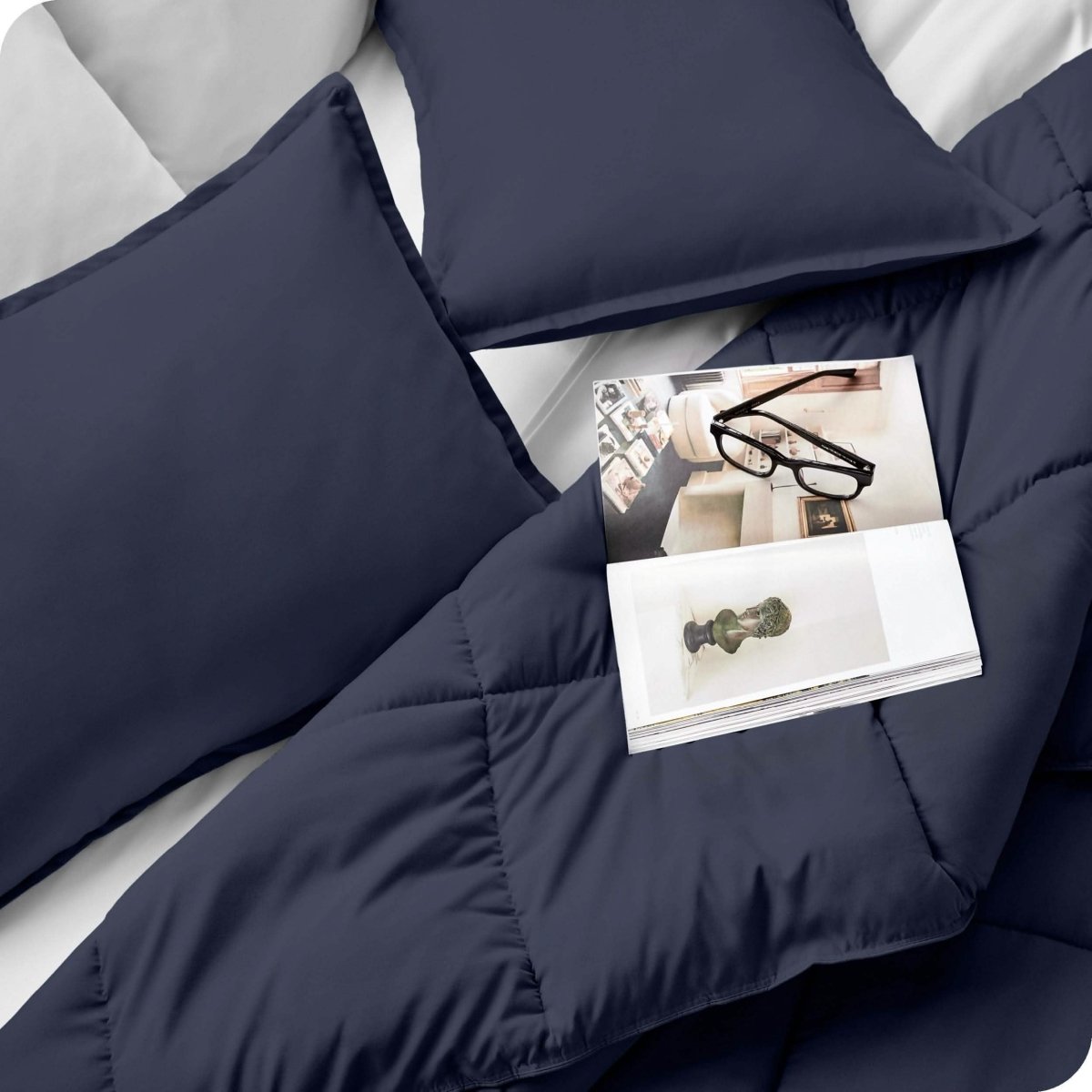 Close up of a comforter set on a bed. There are glasses and a magazine on top of the comforter.