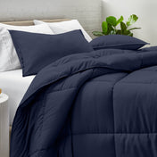 Comforter and pillow shams on a bed with a white brick wall and plant in the background