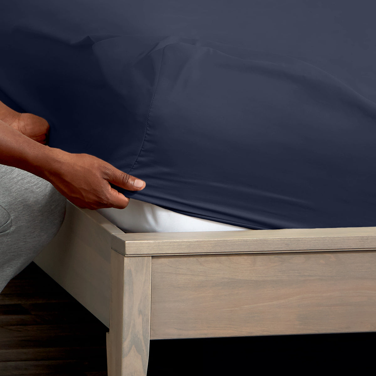 A man is putting a fitted sheet on a bed