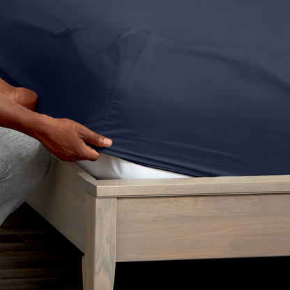 A man is putting a fitted sheet on a bed