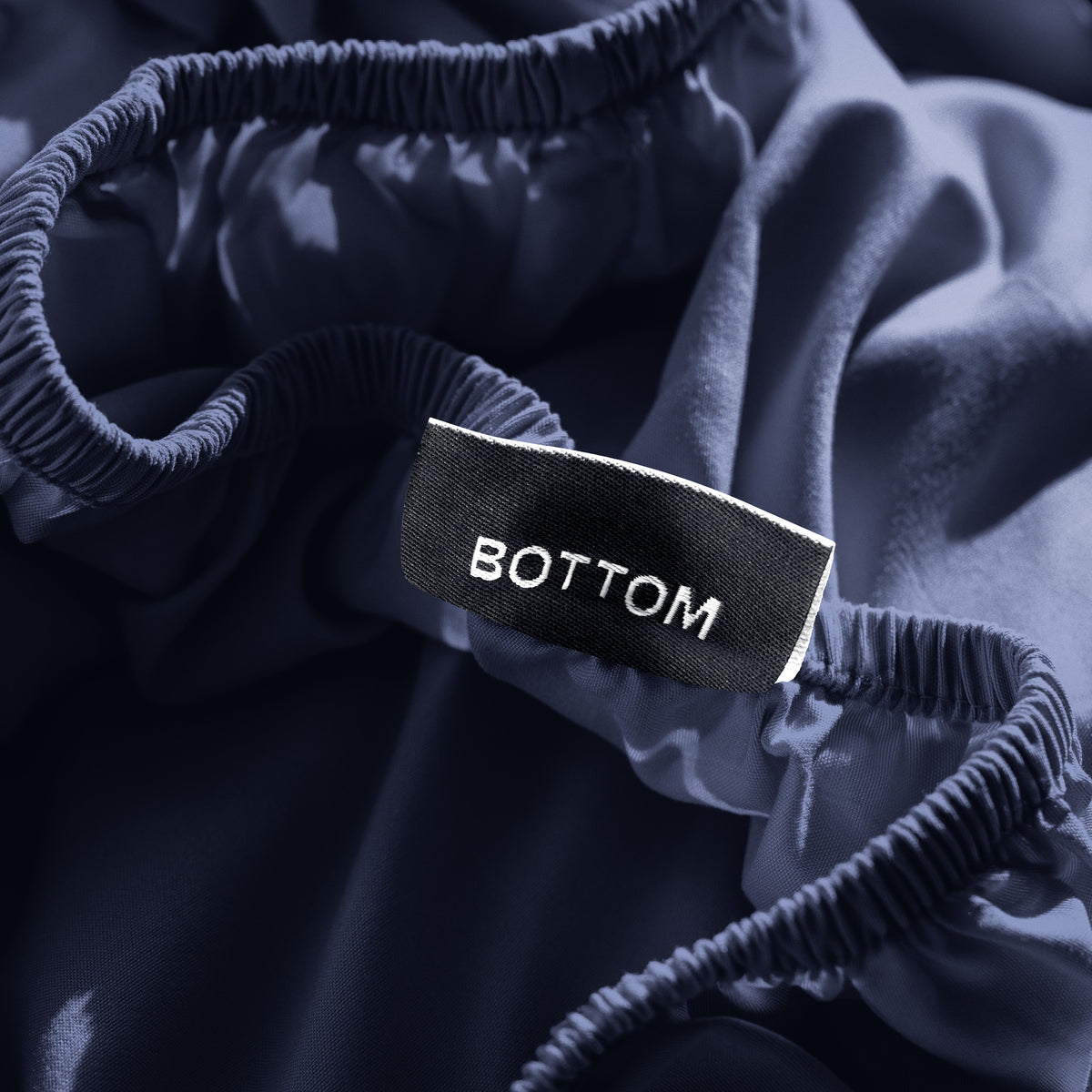 A close-up of a fitted sheet with a label printed with the word 'BOTTOM' in white.