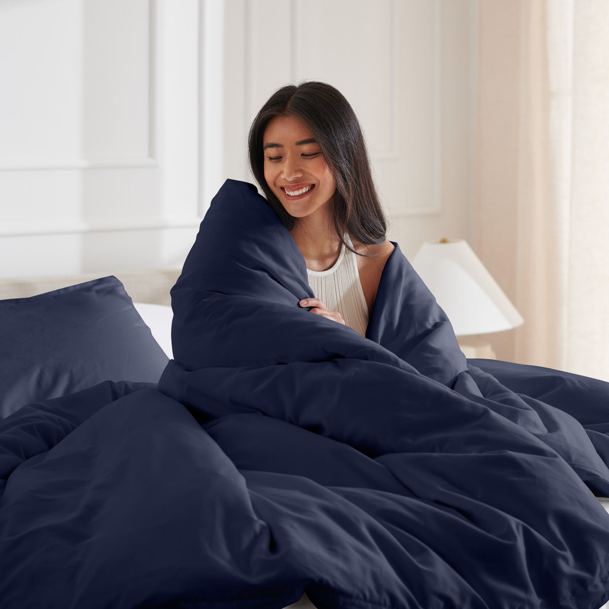 Woman smiling under duvet cover set in a bedroom setting