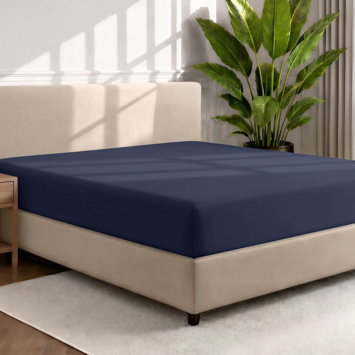 Bed with a fitted sheet in a room with a large plant and rug