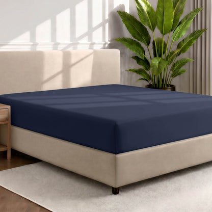 Bed with a fitted sheet in a room with a large plant and rug