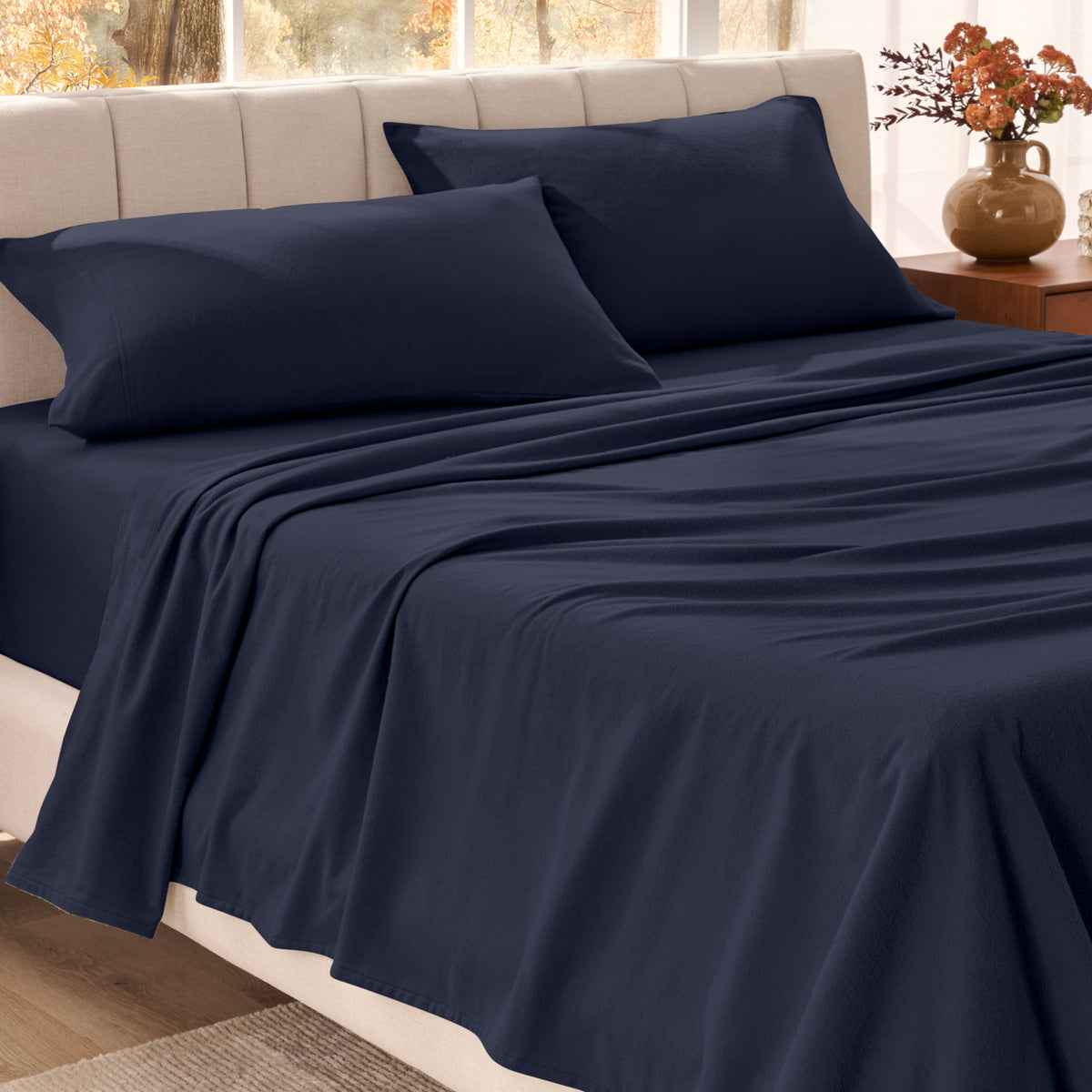Bed sheets on a neatly made bed in a bright bedroom with large windows.