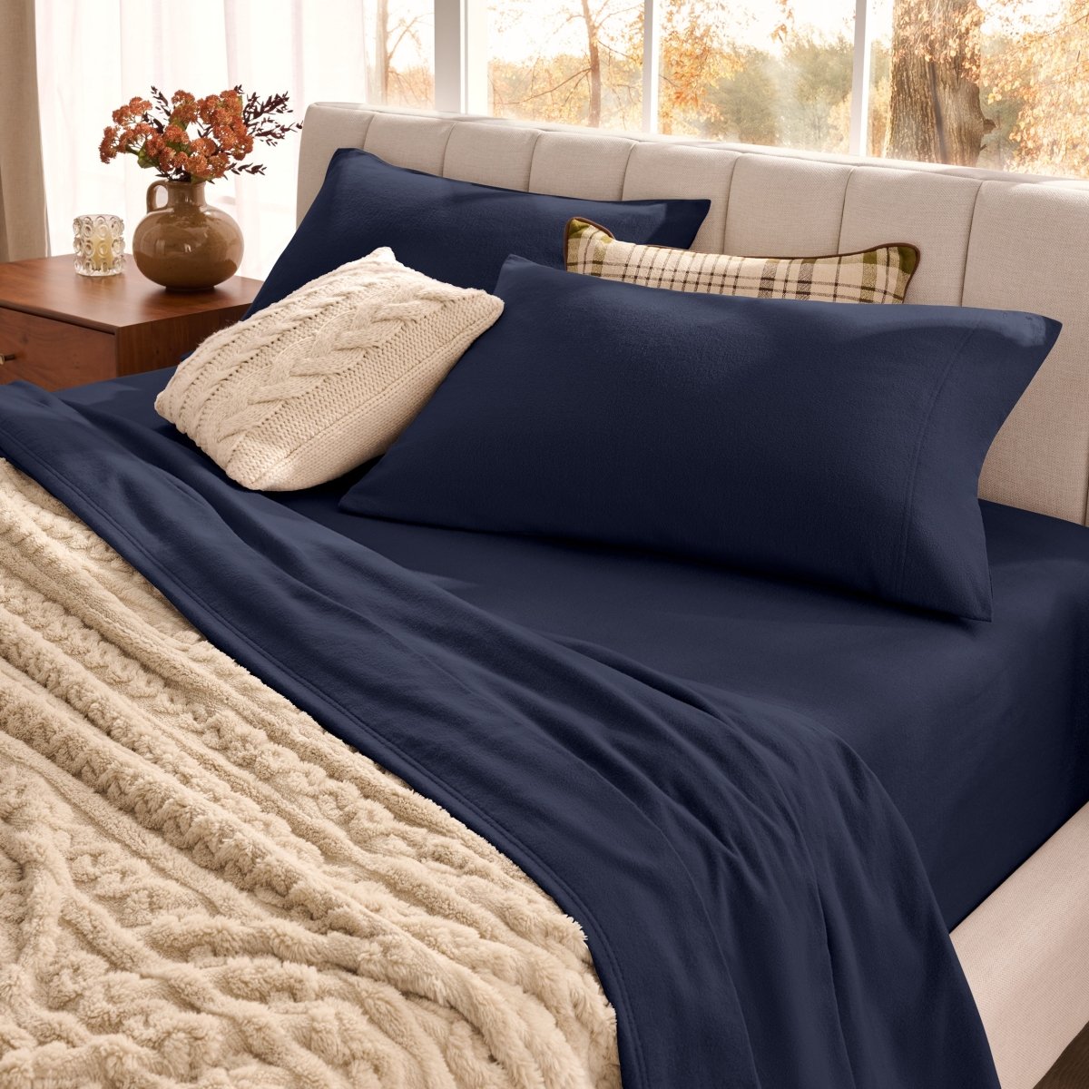 Neatly made bed with organic flannel sheets  and a beige blanket in a bright bedroom.