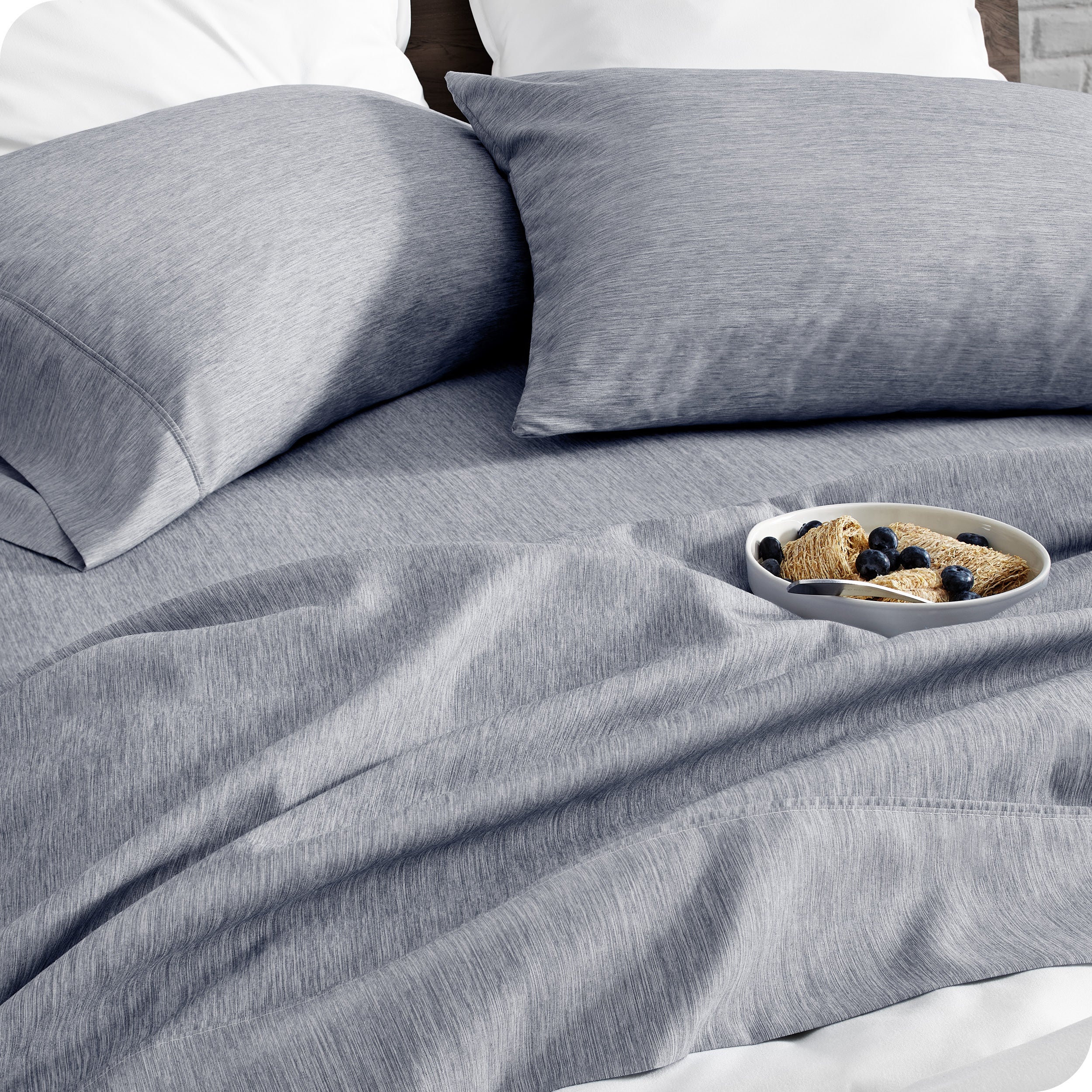 A bed made with sheets. A cereal bowl is on the sheets.
