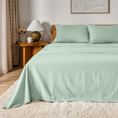 A bed dressed in flannel sheet set in a bedroom with a wooden headboard, bedside table and lamp