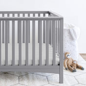 Gray crib with stuffed animals on the floor next to it