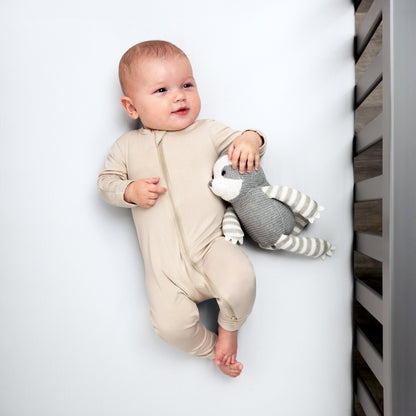Baby in a beige onesie holding a gray and white striped toy while in a crib