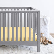 Gray crib with stuffed animals on the floor next to it