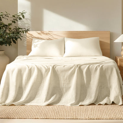 Bed with linen bedding and pillows in a bright room with a plant and lamp.
