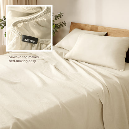 Linen bed sheets and pillowcases on a wooden bed with a plant in the background