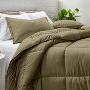 Comforter and pillow shams on a bed with a white brick wall and plant in the background