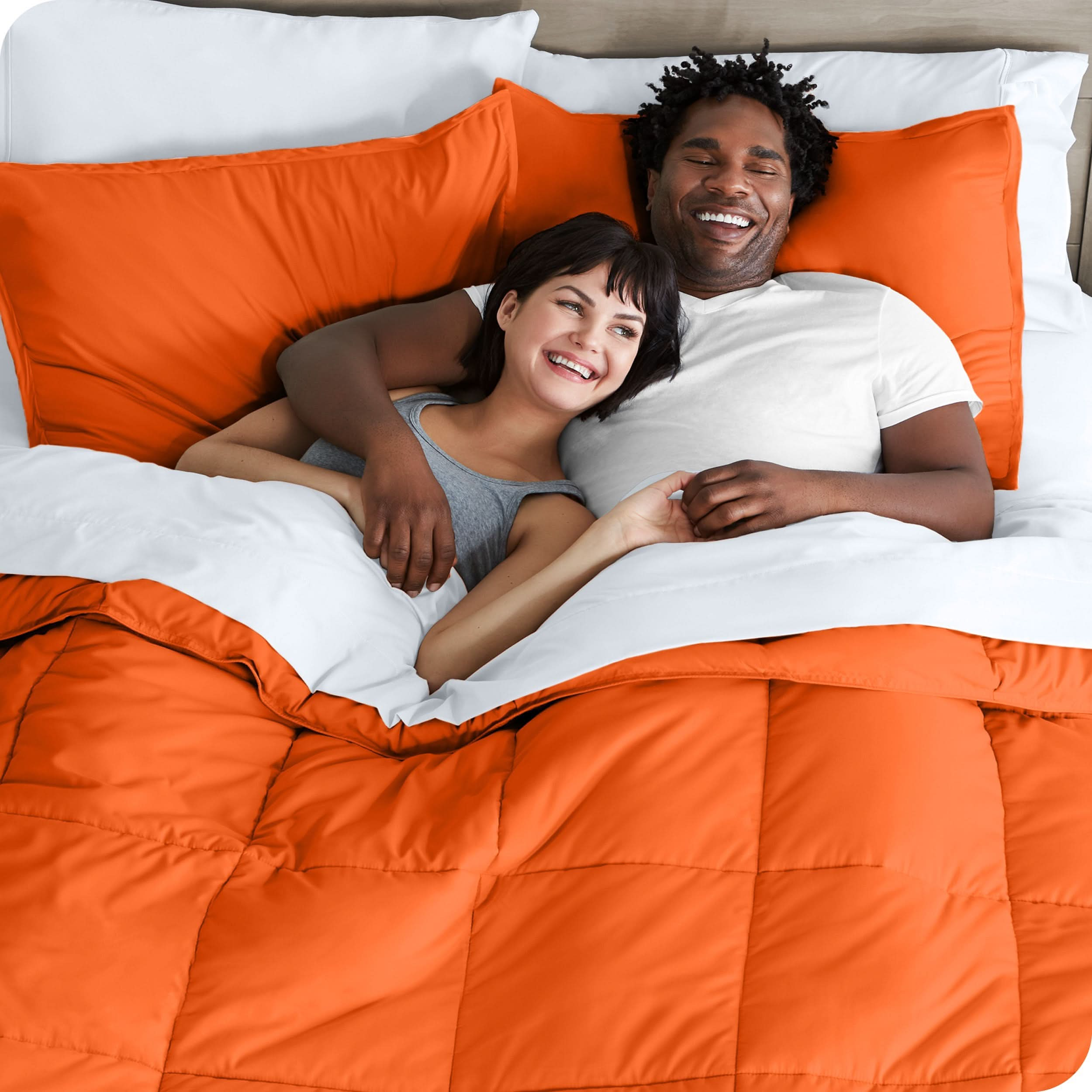 A couple is lying in bed with a comforter and sheets over them