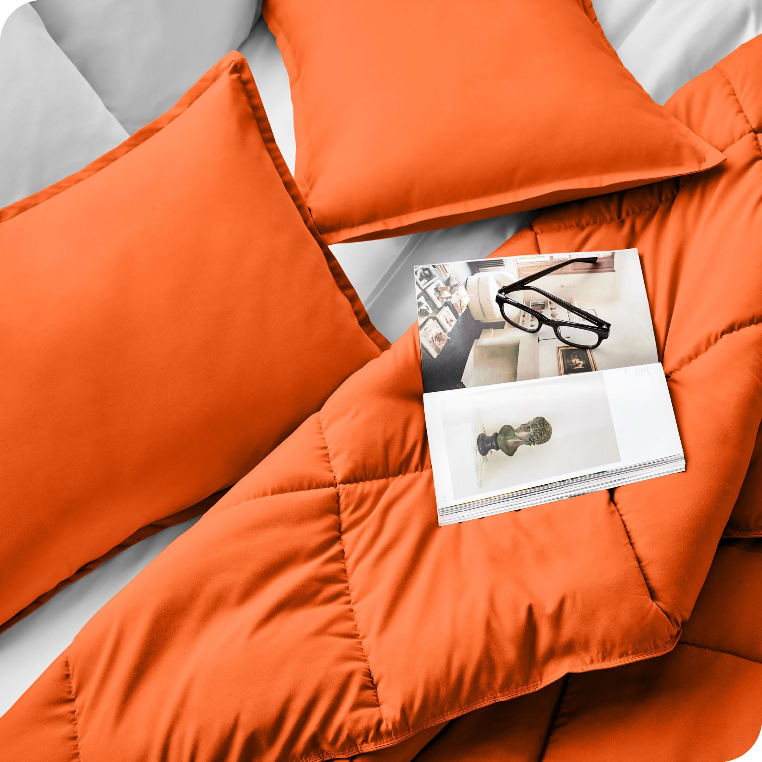 Close up of a comforter set on a bed. There are glasses and a magazine on top of the comforter.