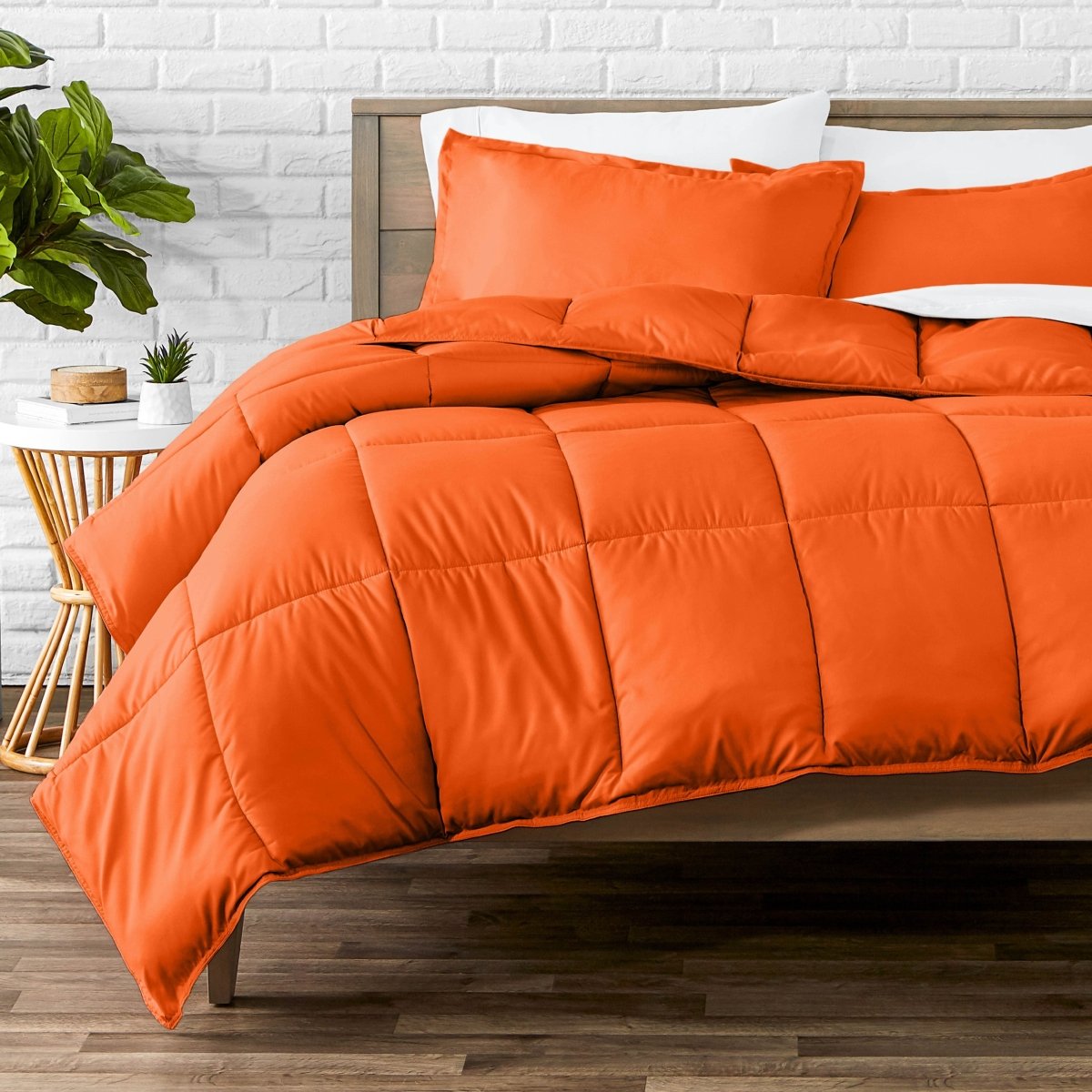 Comforter set on a bed with a white brick wall and plant in the background