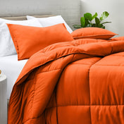 Comforter and pillow shams on a bed with a white brick wall and plant in the background