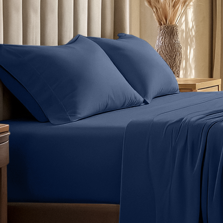 Navy blue bed sheets and pillows on a bed with a beige curtain in the background.