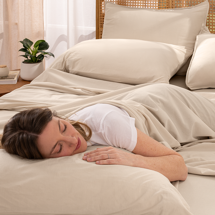 Woman sleeping peacefully in a bed with beige bedding and pillows.