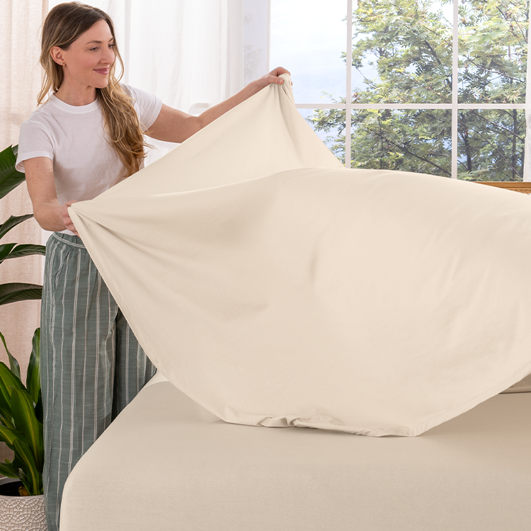 Woman holding a beige pillow in a room with a window and plants