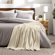 A cotton waffle blanket is on the corner of a bed. It is hanging down the side and end of the bed.