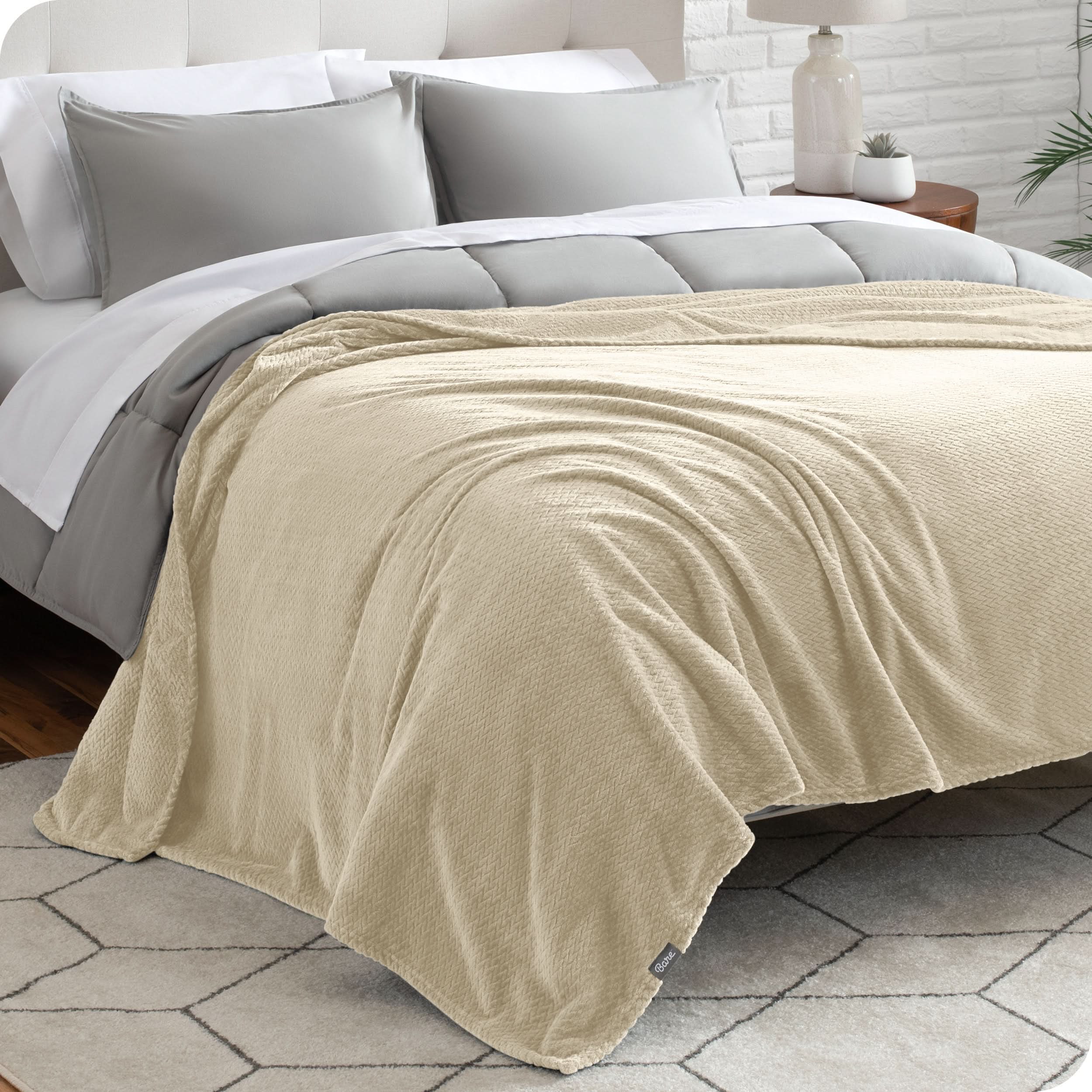 A textured microplush blanket is covering a bed, which has a comforter set on it.