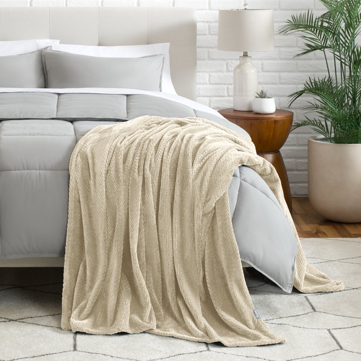 Blanket draped over a bed in a bedroom setting with a lamp and plant.