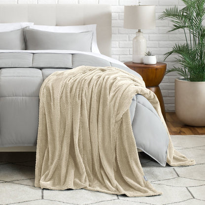 Blanket draped over a bed in a bedroom setting with a lamp and plant.
