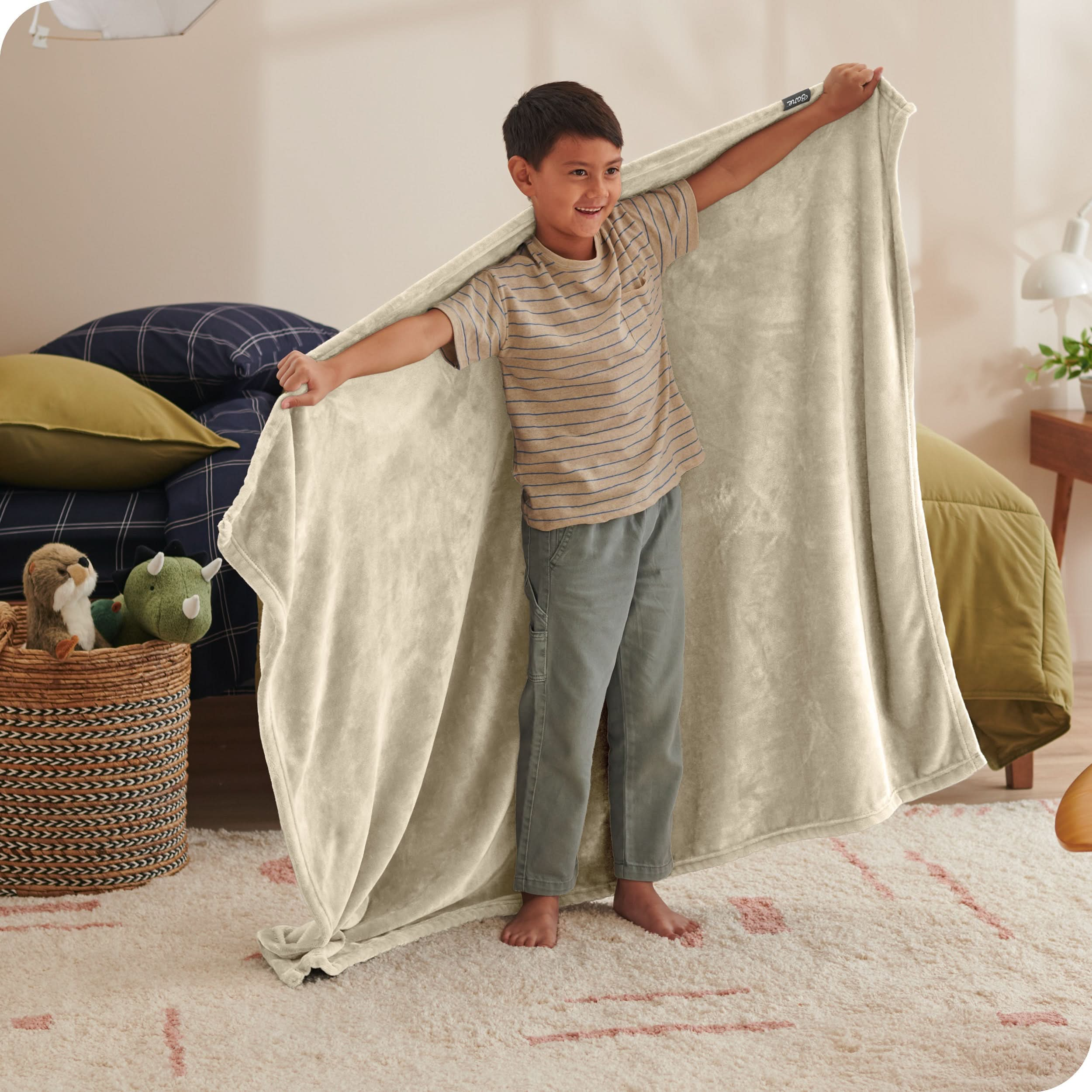 A child has his arms stretched out while holding a microplush blanket behind him