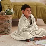 A boy is sitting on the floor of his bedroom with a microplush blanket wrapped around him