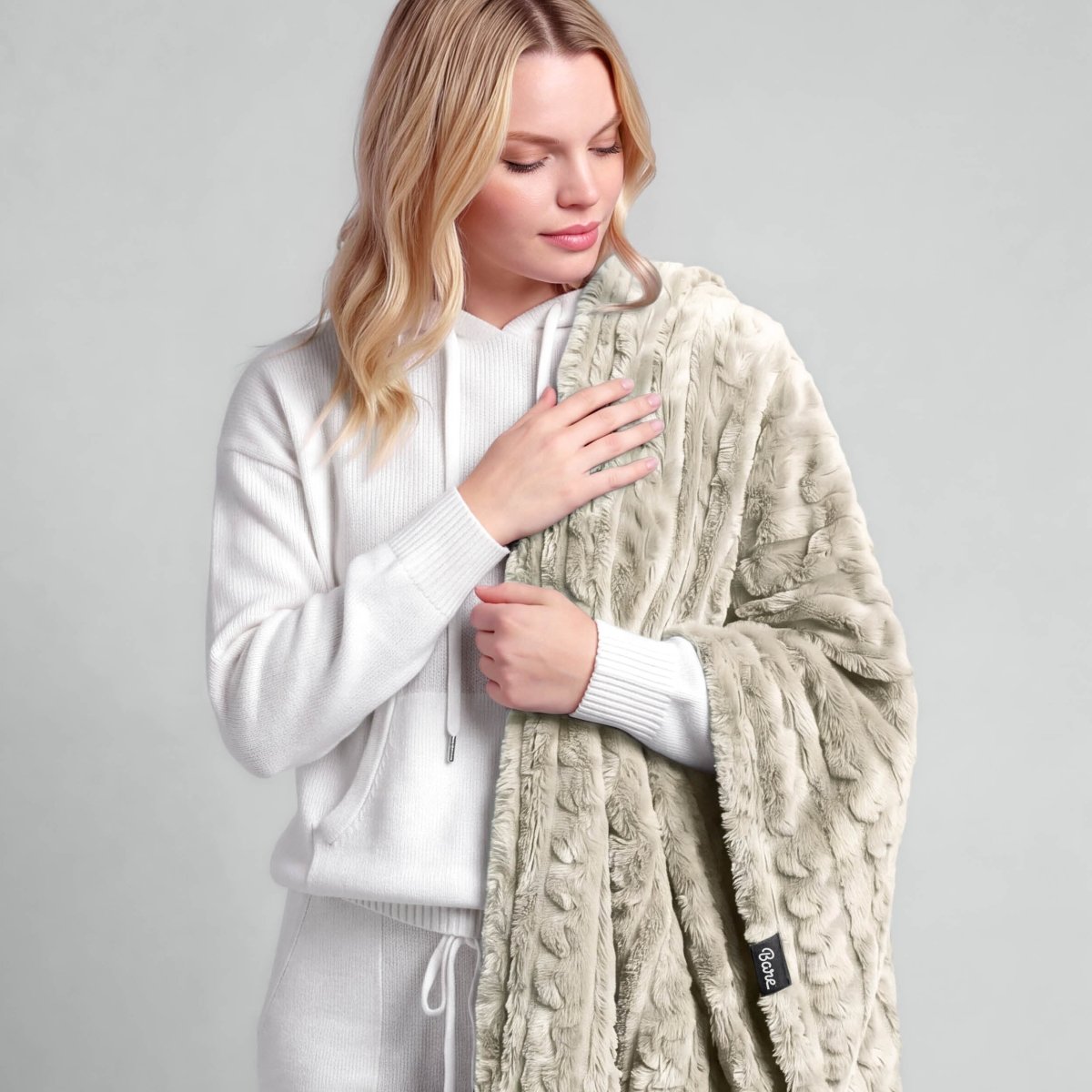 A woman is standing with a textured faux shearling blanket over her shoulder