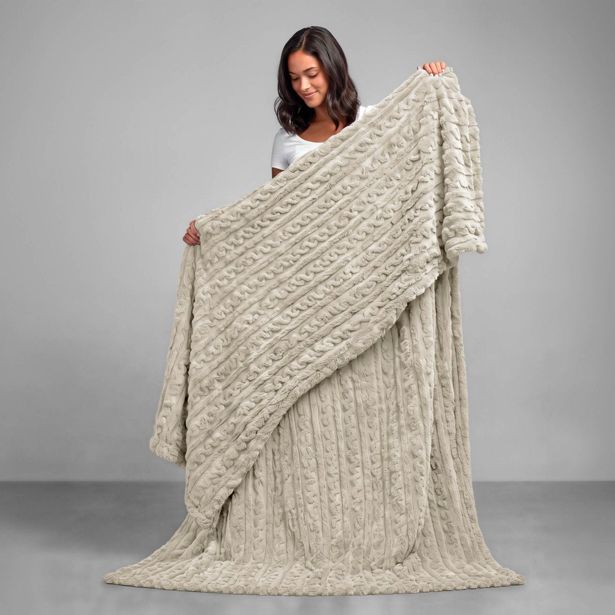 A woman is standing and holding a textured cable knit blanket