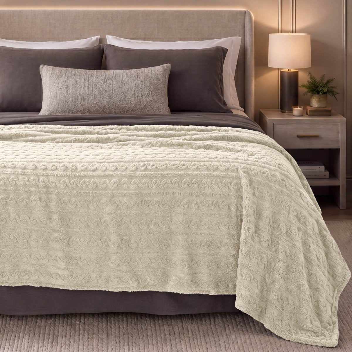 A cable knit blanket draped over the end of a bed