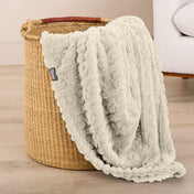 Oyster textured blanket draped over a woven basket on a wooden floor.