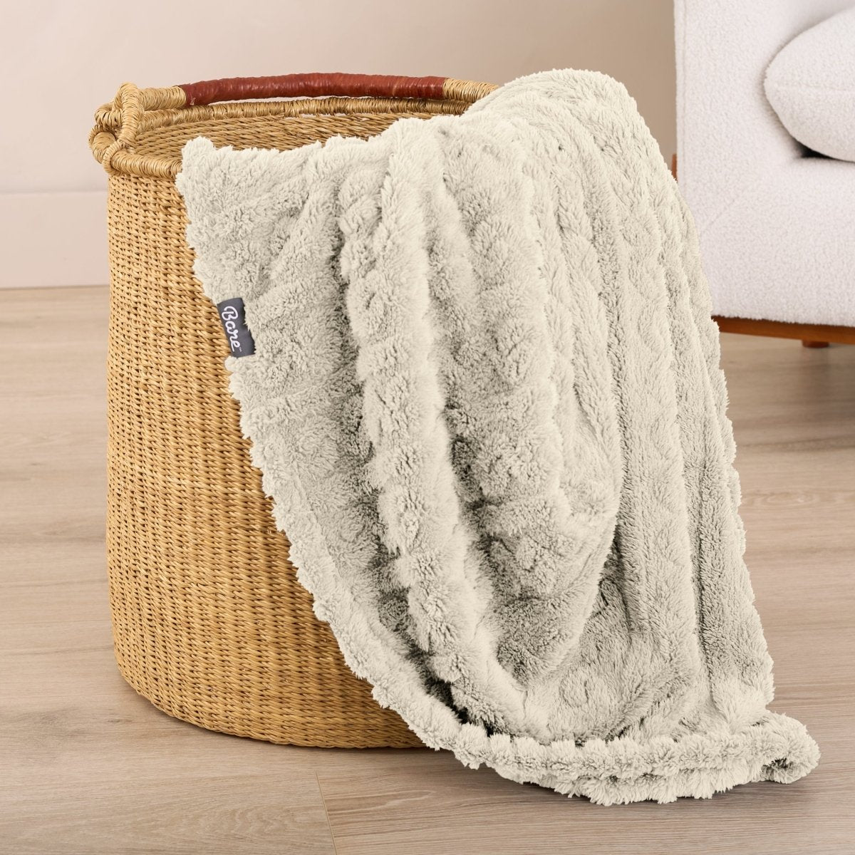 Oyster textured blanket draped over a woven basket on a wooden floor.
