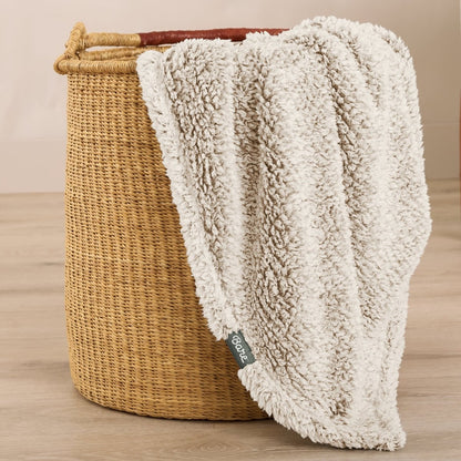Textured blanket draped over a wicker basket on a wooden surface