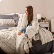 A woman sitting on the end of a bed with a shaggy blanket wrapped around her