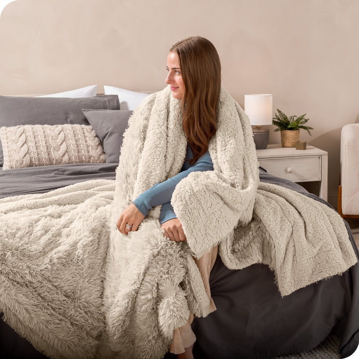 A woman sitting on the end of a bed with a shaggy blanket wrapped around her
