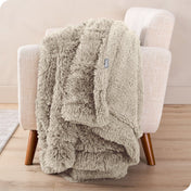 A woman sitting on the end of a bed with a shaggy blanket wrapped around her