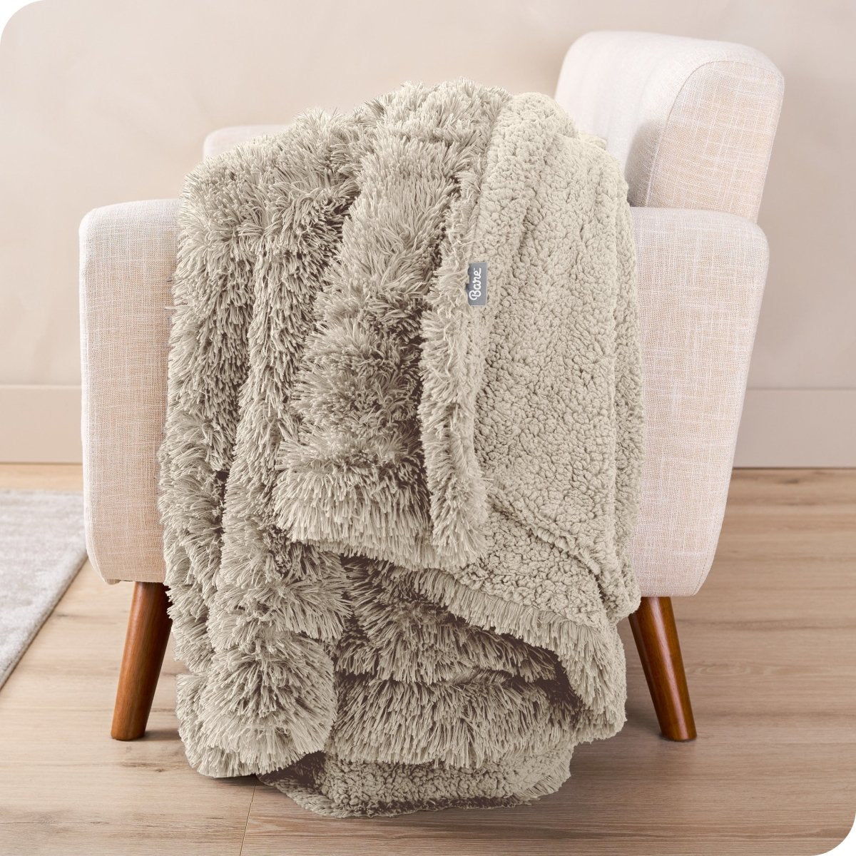 A woman sitting on the end of a bed with a shaggy blanket wrapped around her