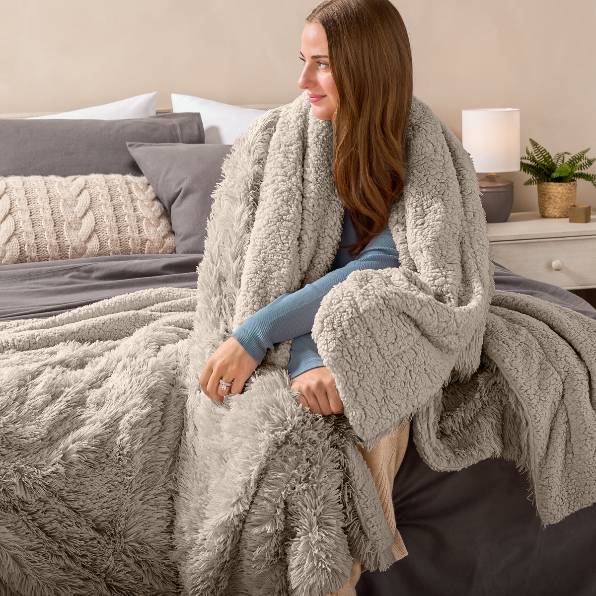 Fluffy blanket draped over a woman sitting on the end of a bed