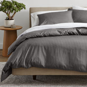 A bed dressed in a gray and white pinstriped duvet cover and matching pillow shams.