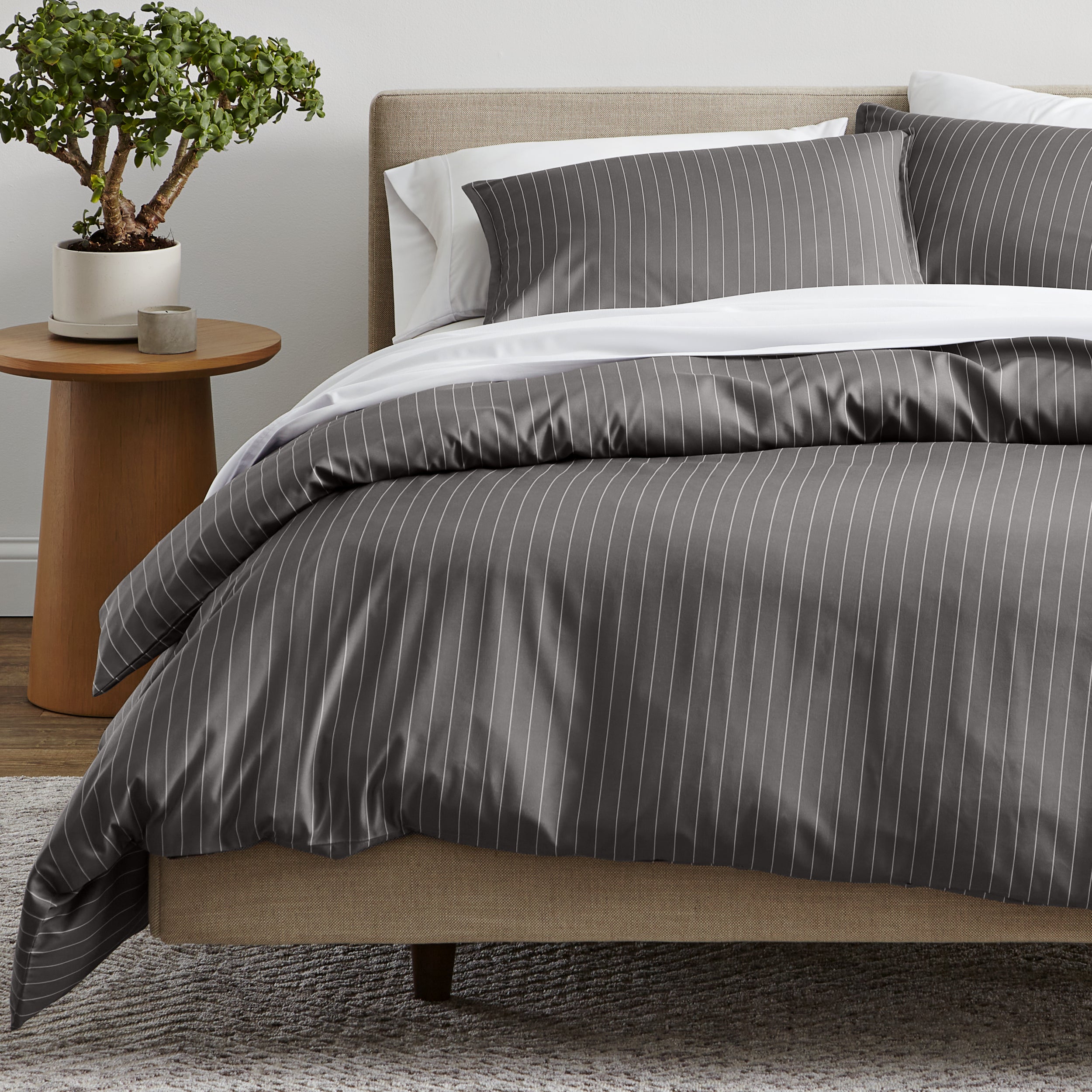 A bed dressed in a gray and white pinstriped duvet cover and matching pillow shams.