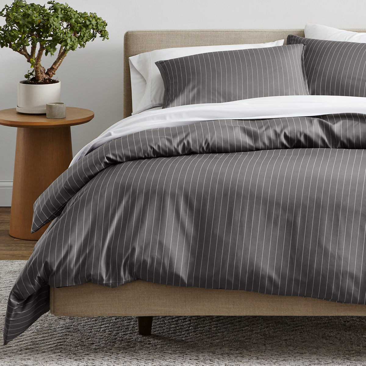 A bed dressed in a gray and white pinstriped duvet cover and matching pillow shams.