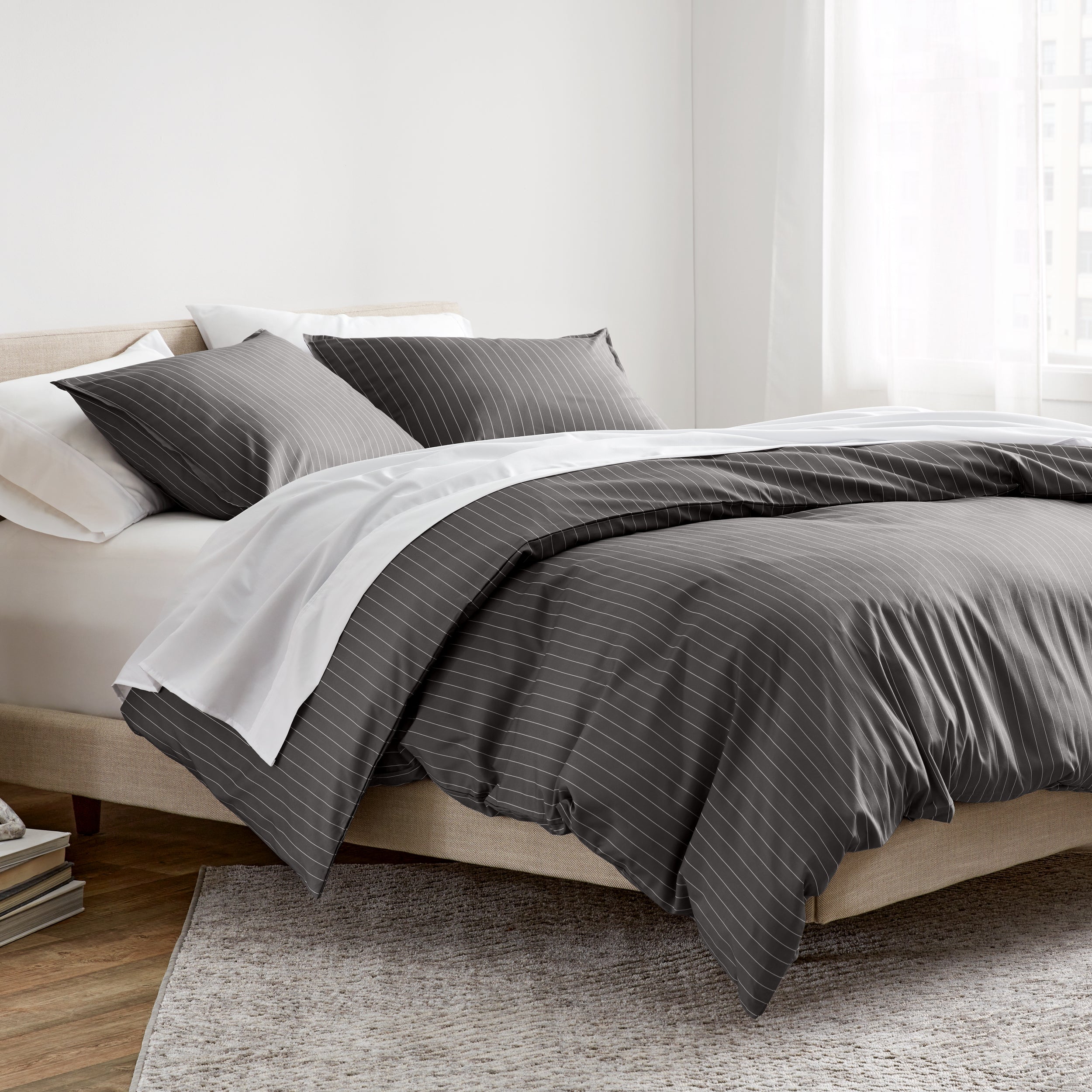 A neatly made bed in a bright bedroom setting, featuring a dark gray and white striped duvet cover.