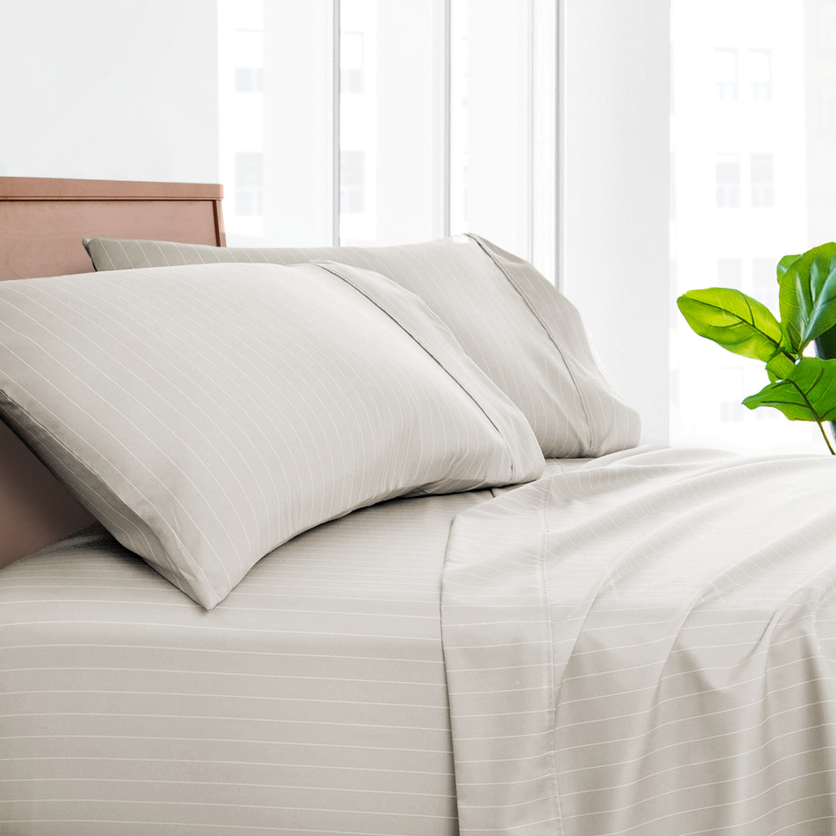 A neatly made bed with light beige striped sheets and matching pillowcases