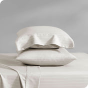 Two pillows with pillowcases on them stacked on a bed